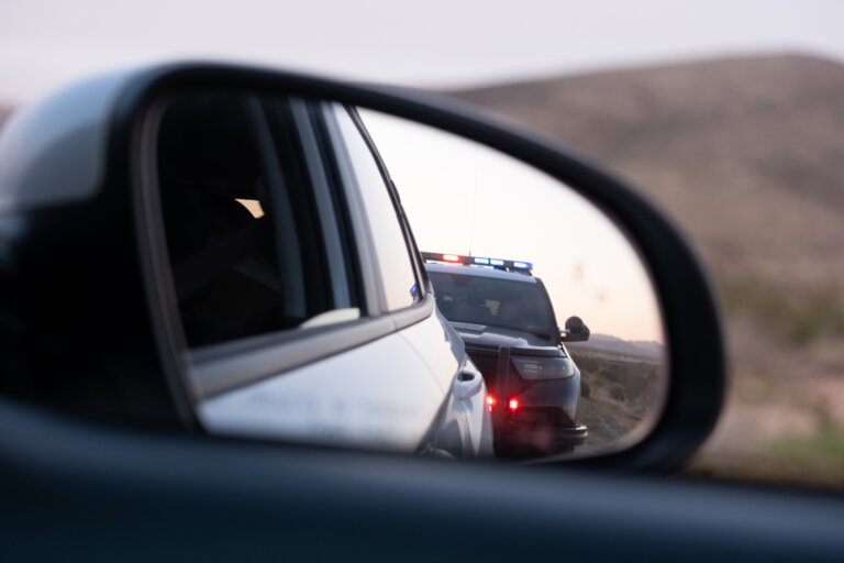 Police SUV with flashing lights seen in a car’s side mirror